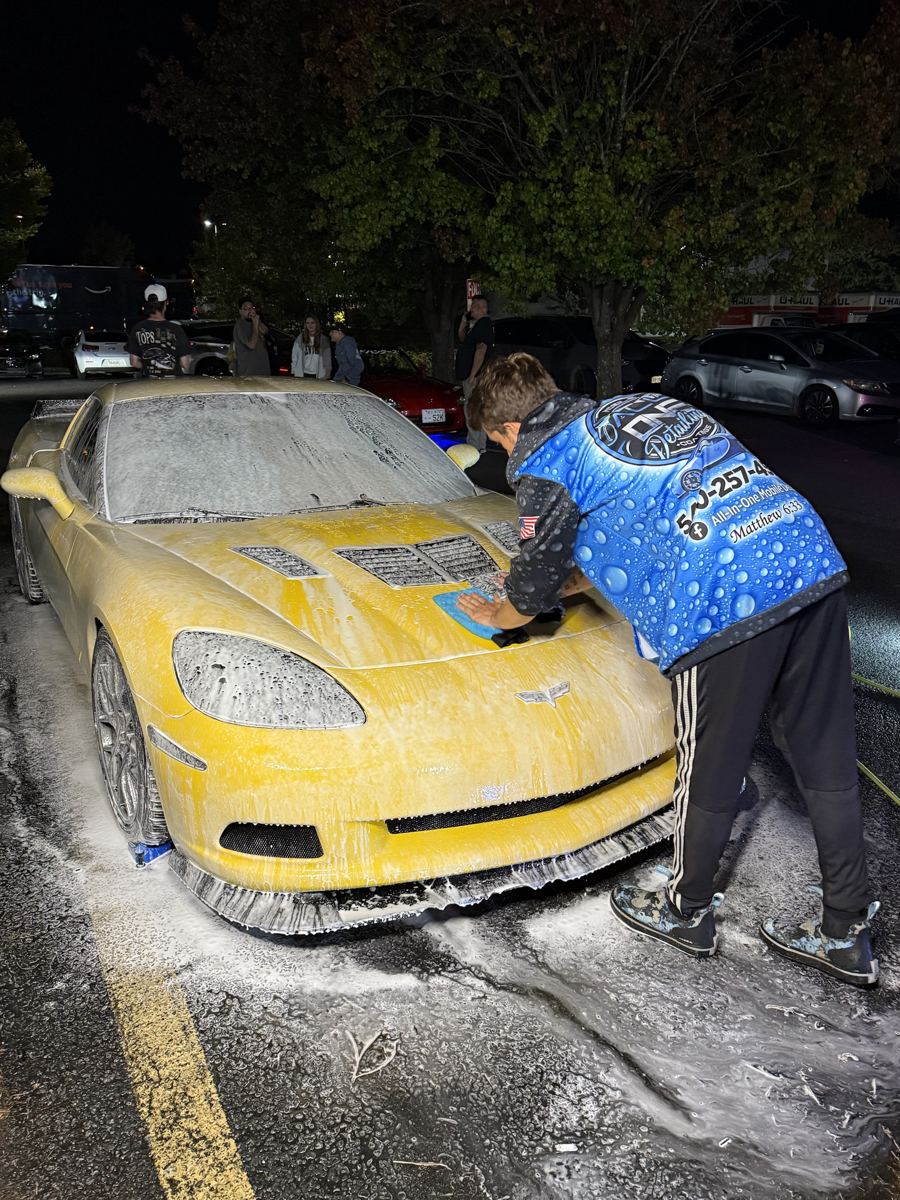 A detailer hand washing a foamed Corvette